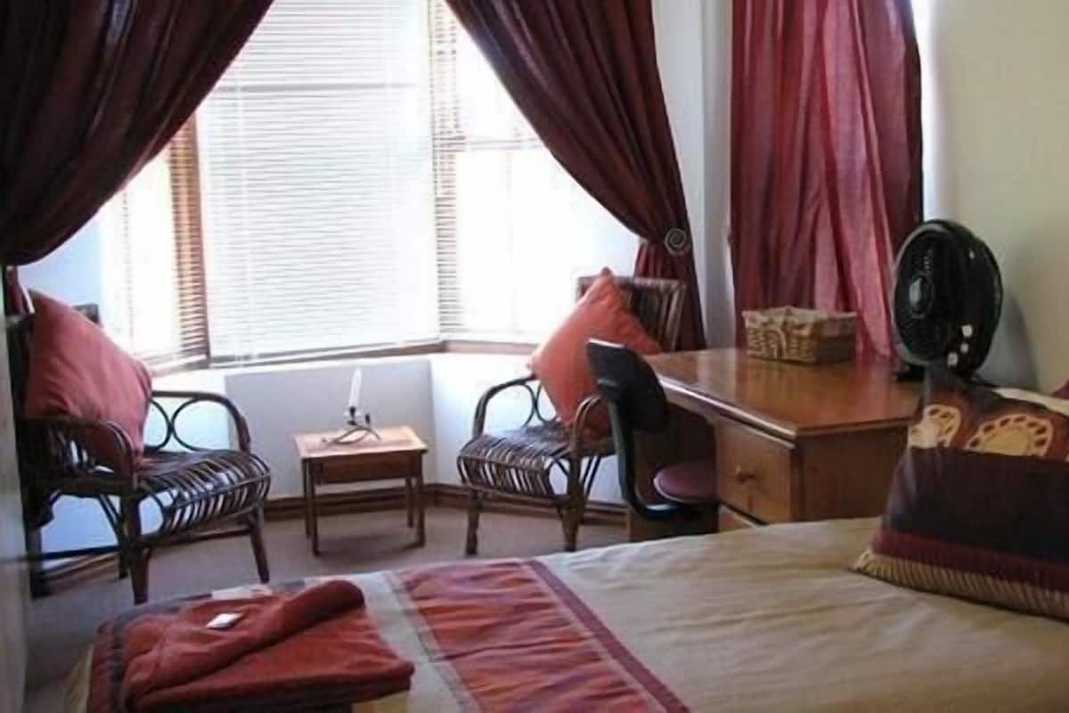 A hotel room with a bed, a desk, two chairs, a small table, and a fan.