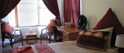 Une chambre d’hôtel avec un lit, un bureau, deux chaises, une petite table et un ventilateur.