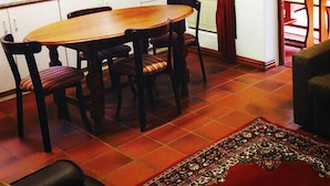 A dining area with a wooden table and chairs, a kitchen with a microwave, and a red curtain. - Magnolia Place Guest House (Stellenbosch)