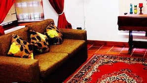 A living room with a sofa, red curtains, a flat-screen TV, a small table with bottles, and a patterned rug. - Magnolia Place Guest House (Stellenbosch)