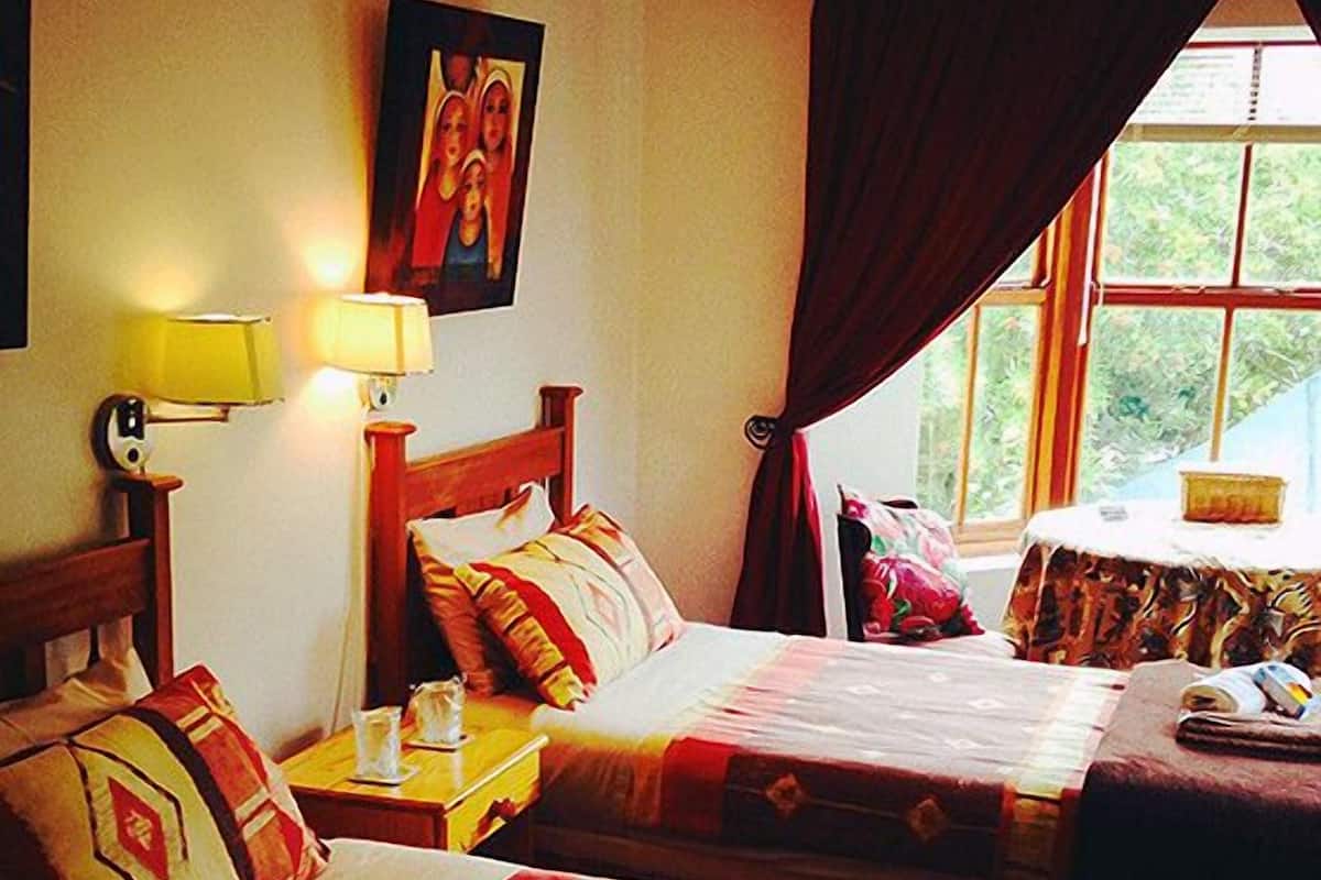 A hotel room with two beds, a nightstand with a lamp, a window with curtains, and a painting on the wall.