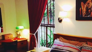 A hotel room with a bed, a nightstand, a lamp, a window with curtains, and a wall-mounted light. - Magnolia Place Guest House (Stellenbosch)