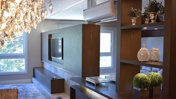 Un salon moderne doté d’un téléviseur à écran plat fixé au mur, d’étagères intégrées ornées d’objets décoratifs et d’une grande fenêtre laissant entrer la lumière naturelle.