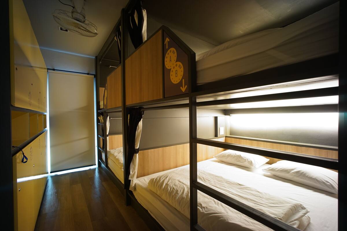 Een slaapkamer met een stapelbed, een houten hoofdbord, een plafondventilator en een raam met jaloezieën.
