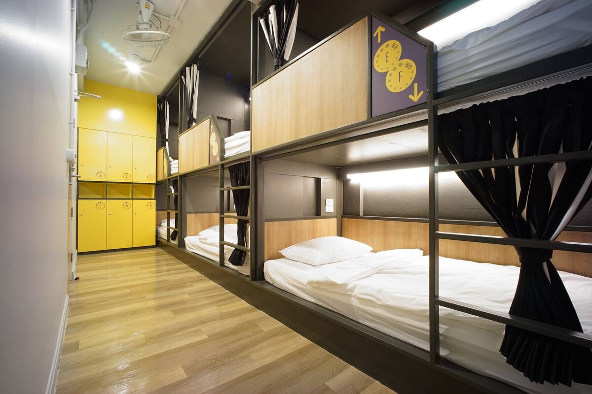 Een slaapzaal met stapelbedden, een houten vloer en een gele wand.