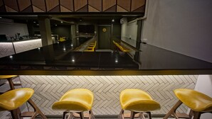 A modern bar area with a long counter, yellow bar stools, and a herringbone-patterned wall. - BRB Hostel Bangkok Silom (Bangkok)