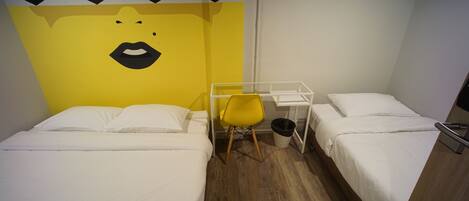 Une chambre d’hôtel avec deux lits, une chaise jaune, un bureau blanc et un mur orné d’un motif noir et blanc.