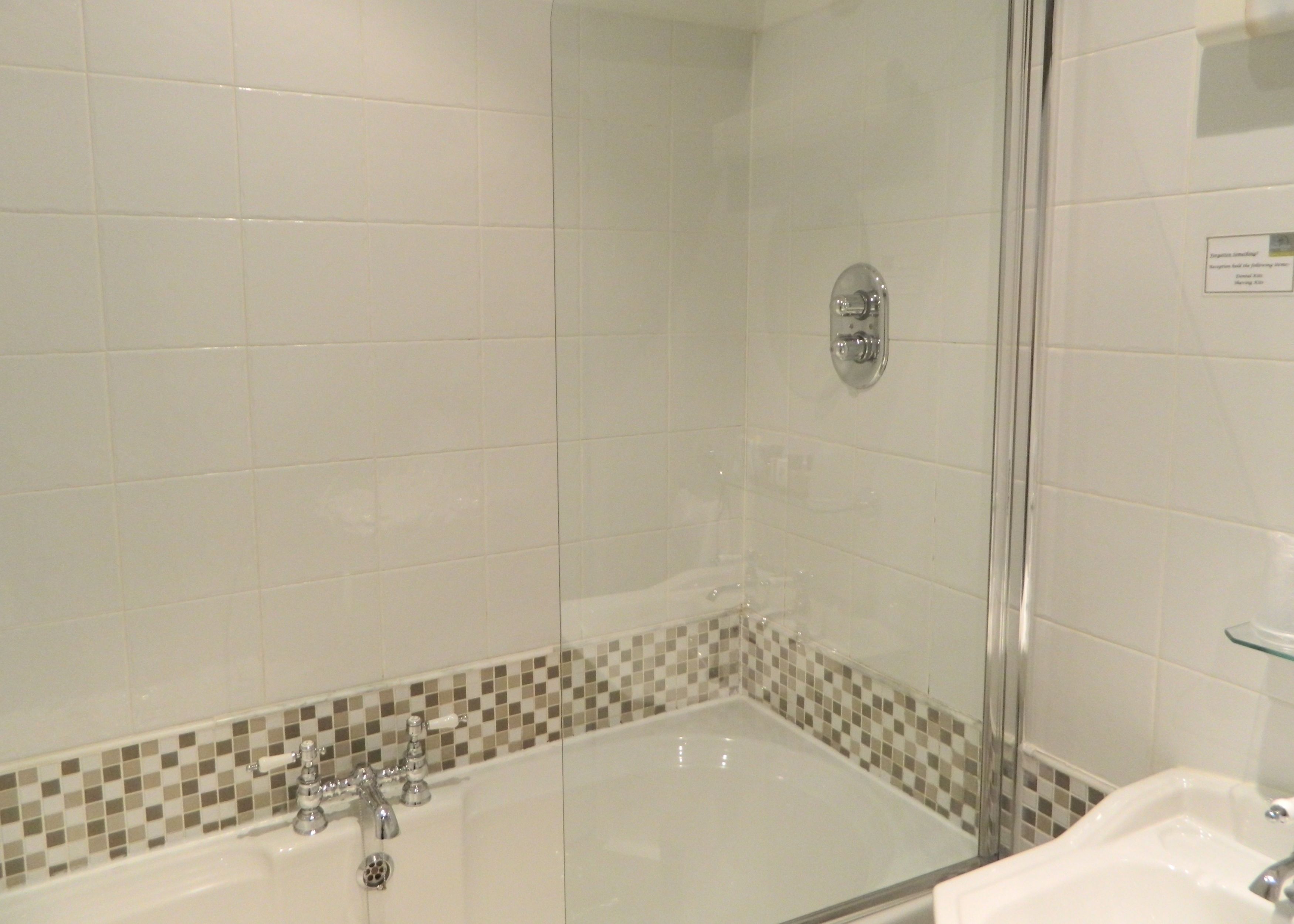 A bathroom with a glass-enclosed shower, a bathtub with a checkered tile border, and a white sink.