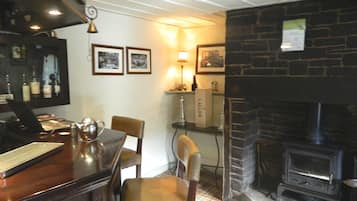 Zona de bar con mostrador de madera, sillas, chimenea y cuadros en la pared.