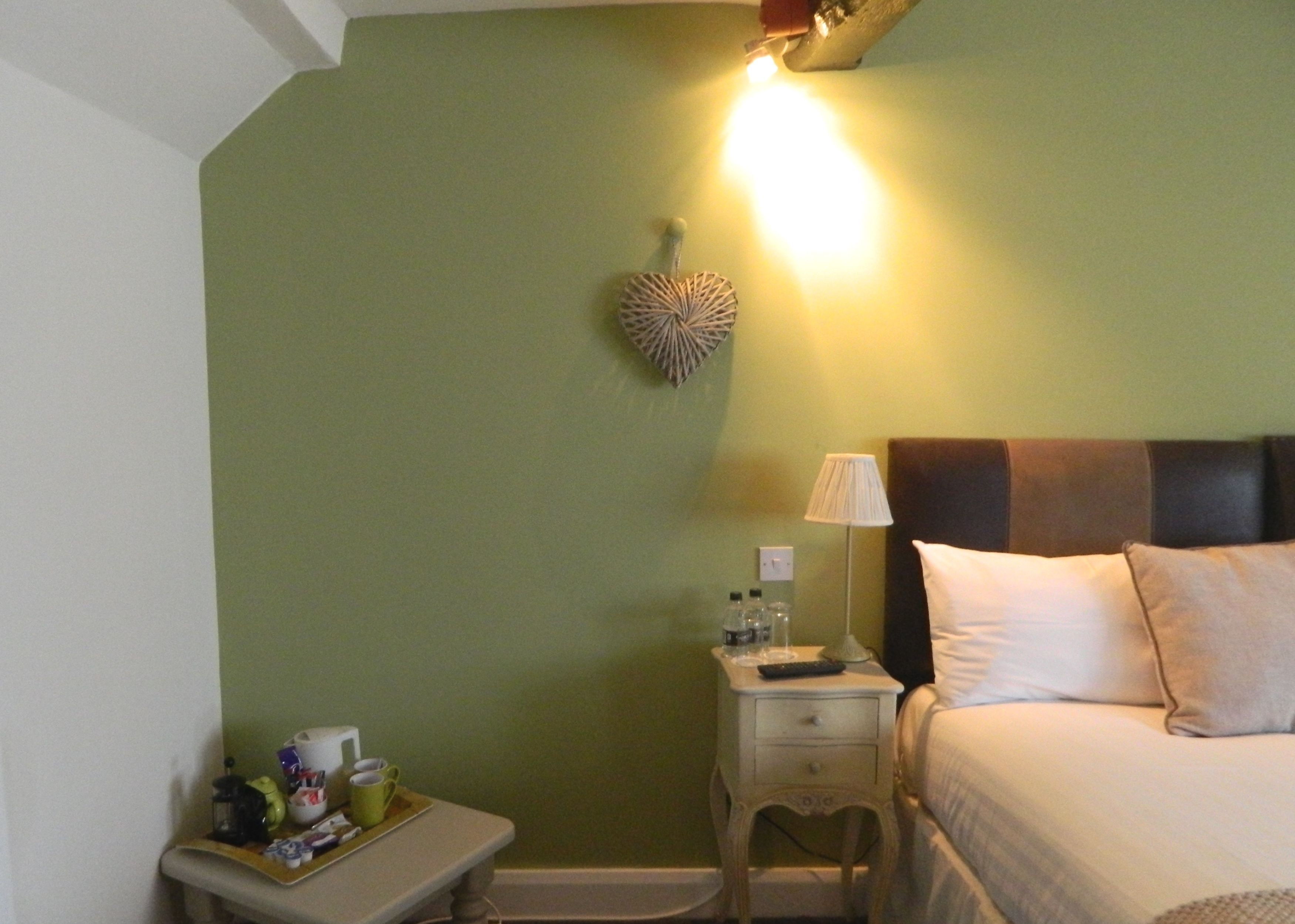 A hotel room with a bed, bedside table, lamp, and a wall decoration.