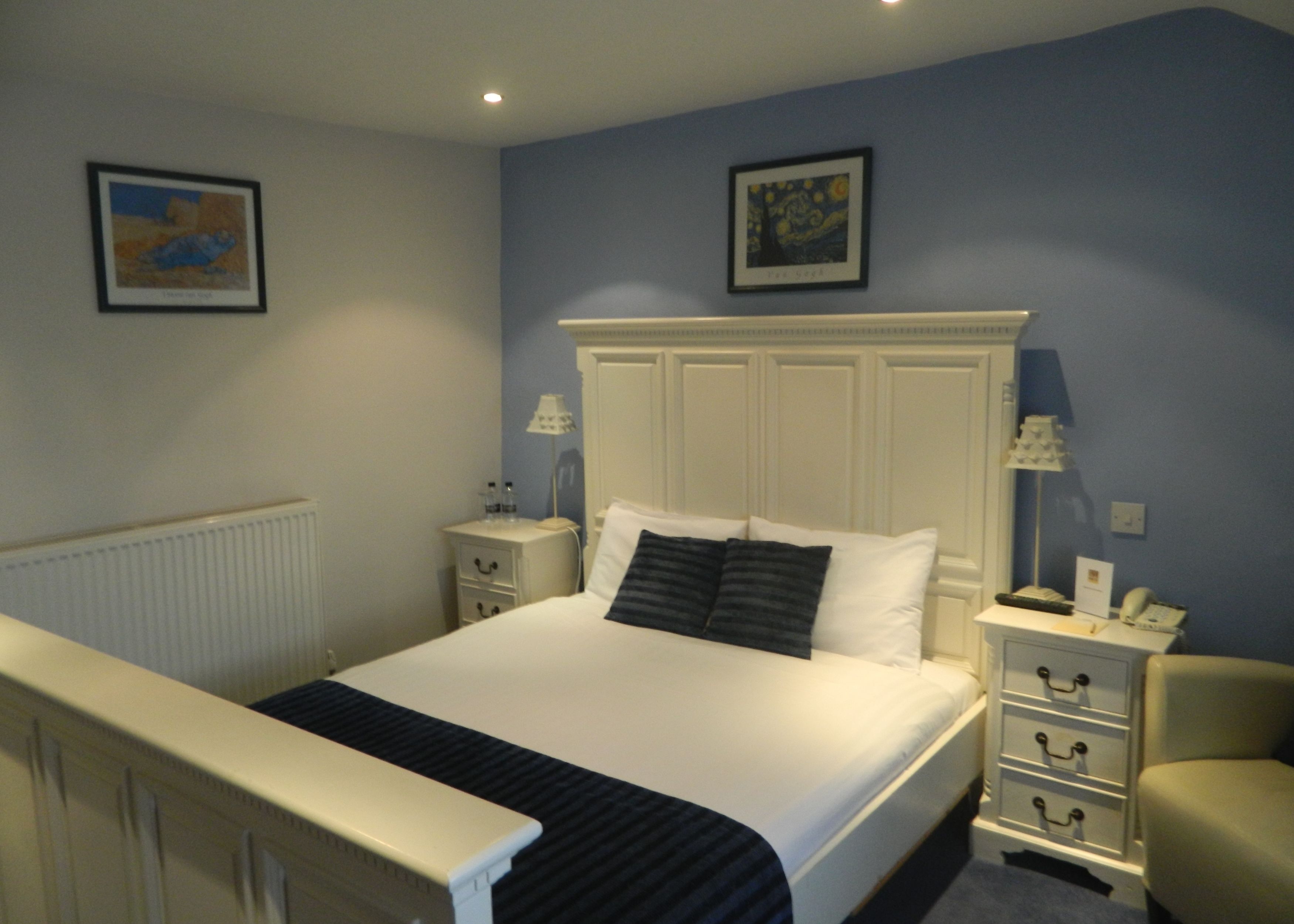 A bedroom with a bed, bedside tables, a chair, and two framed artworks on the walls.