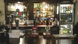 Una zona de bar con varias estanterías llenas de botellas, un grifo etiquetado como "Yorkshire Pale" y un atril para el menú.