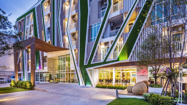 Un hotel moderno con una facciata geometrica originale, area salotto esterna e un giardino curato.