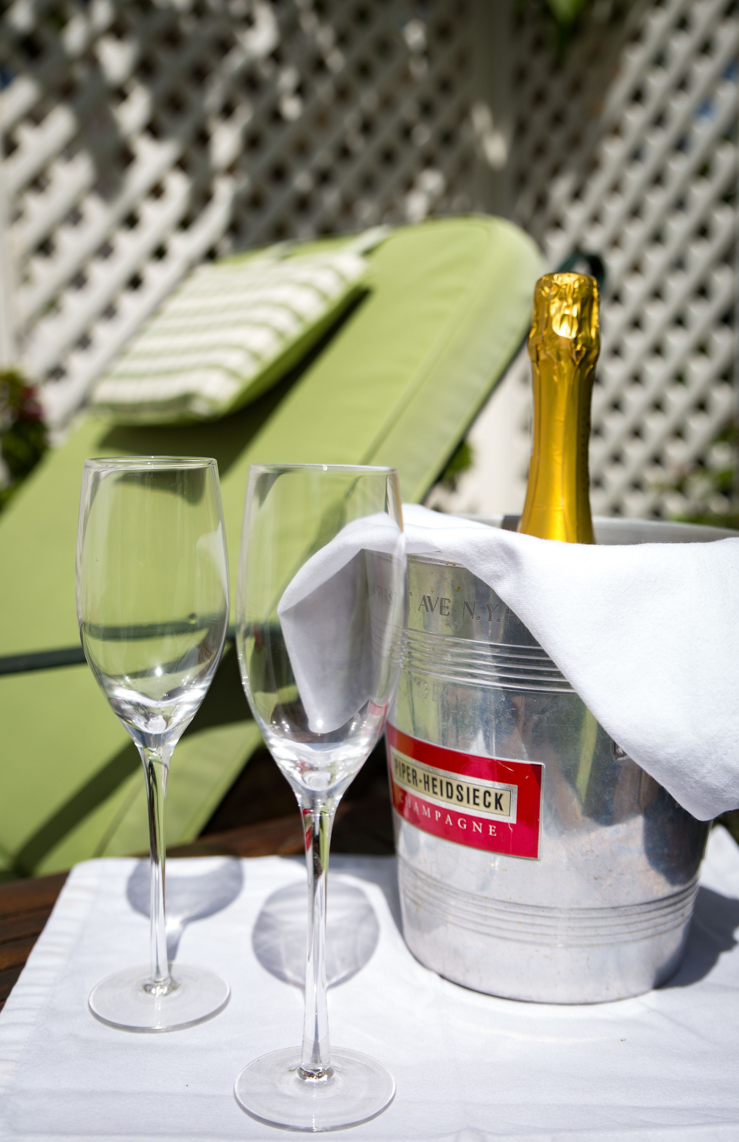 A bottle of champagne in a bucket with a label, two empty wine glasses, and a white tablecloth.