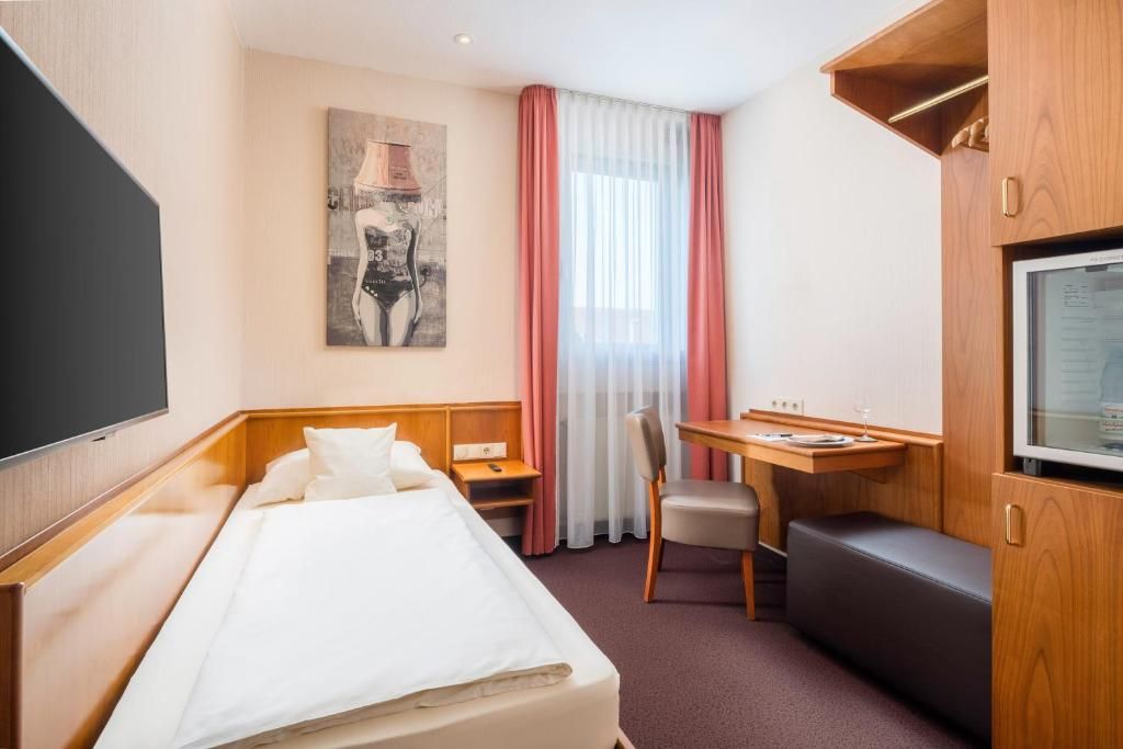 A hotel room with a bed, a desk, a chair, a television, and a painting on the wall.