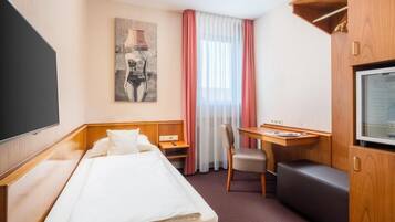 A hotel room with a bed, a desk, a chair, a television, and a painting on the wall.