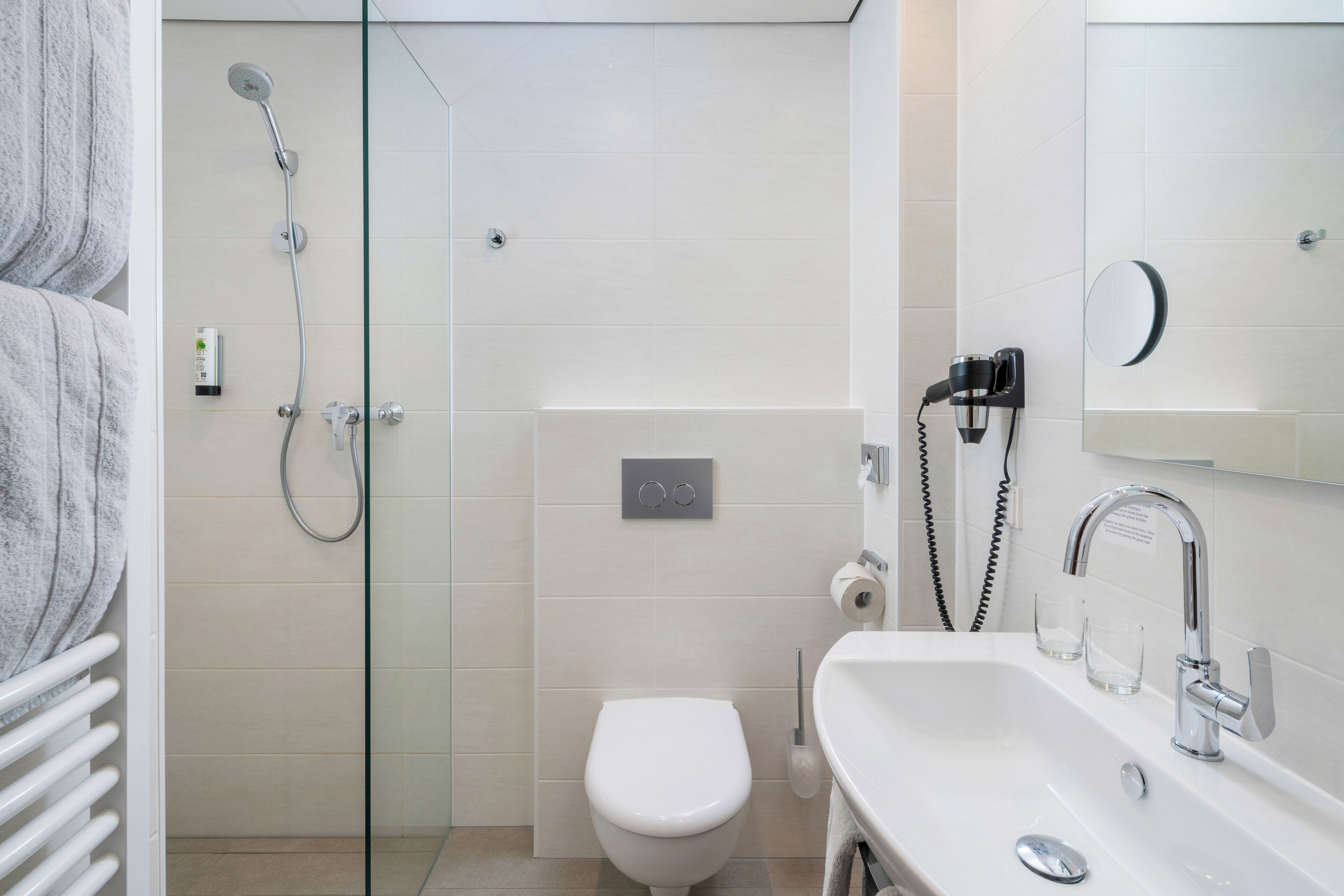 Ein modernes Badezimmer mit Duschkabine aus Glas, einer weißen Toilette, einem Waschbecken mit Spiegel und einem Handtuchhalter.
