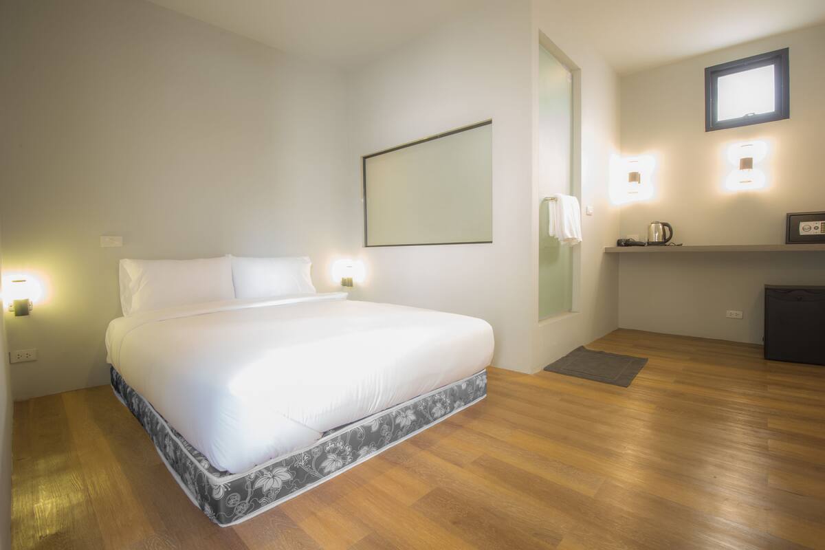 A bedroom with a bed, bedside lamps, a small table with a kettle, and a mirror on the wall.
