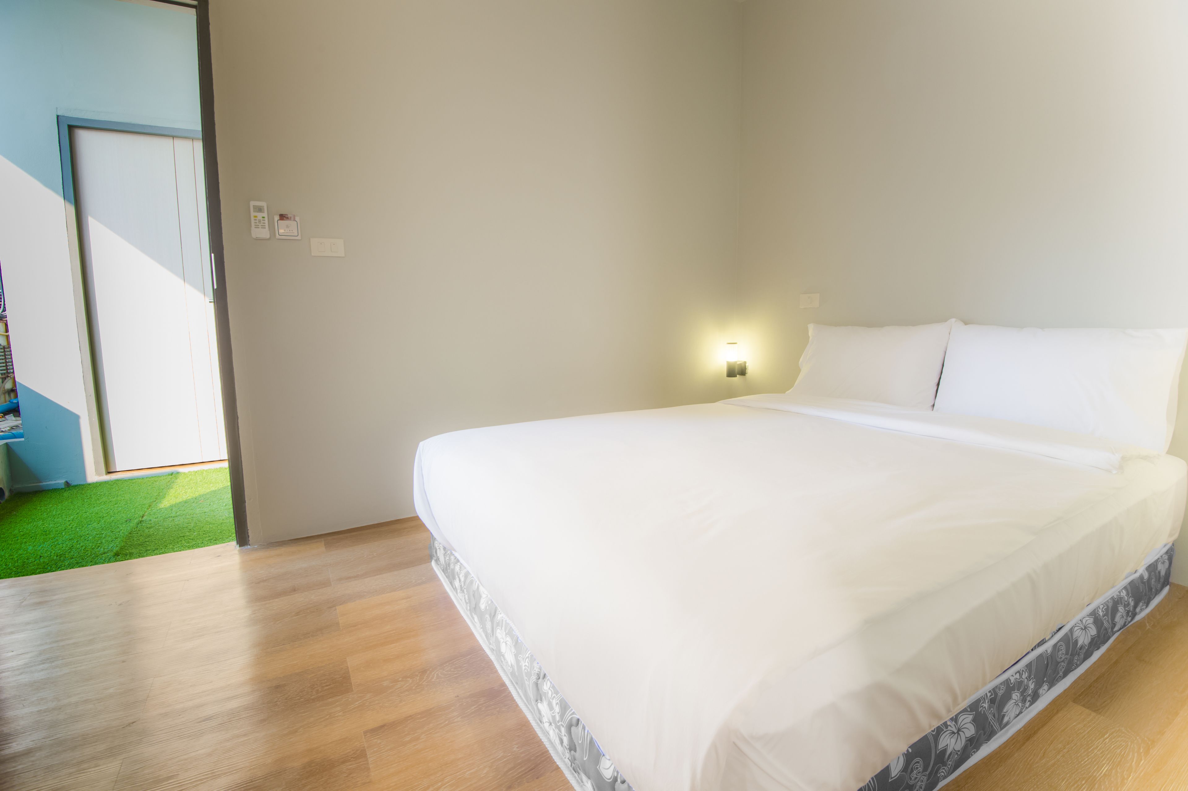 A bedroom with a large bed, a wall-mounted light, and a door leading to a green area.