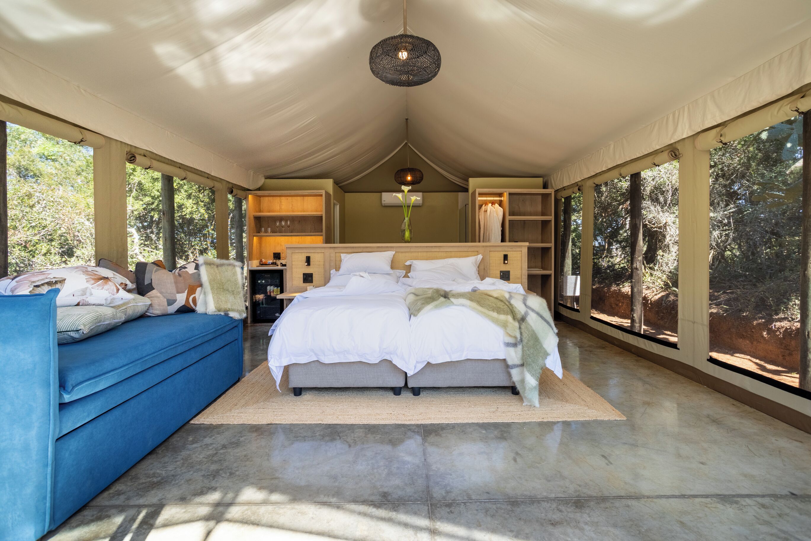 A tented accommodation with a bed, a blue sofa, and a view of the outdoors.