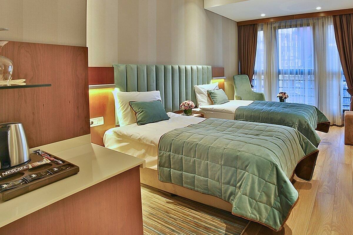 A hotel room with two beds, a minibar, a seating area, and a large window with curtains.