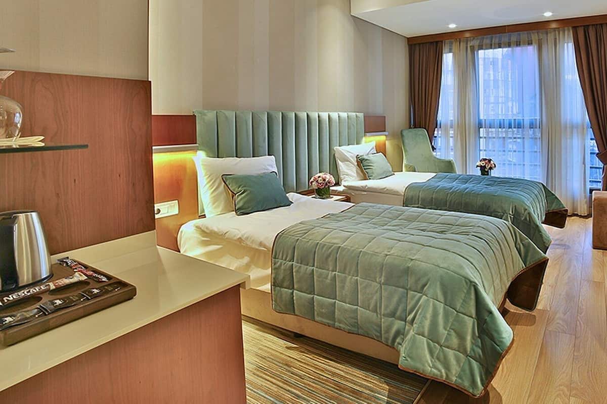 Hotelkamer met twee bedden, een minibar, een zithoek en een groot raam met gordijnen.
