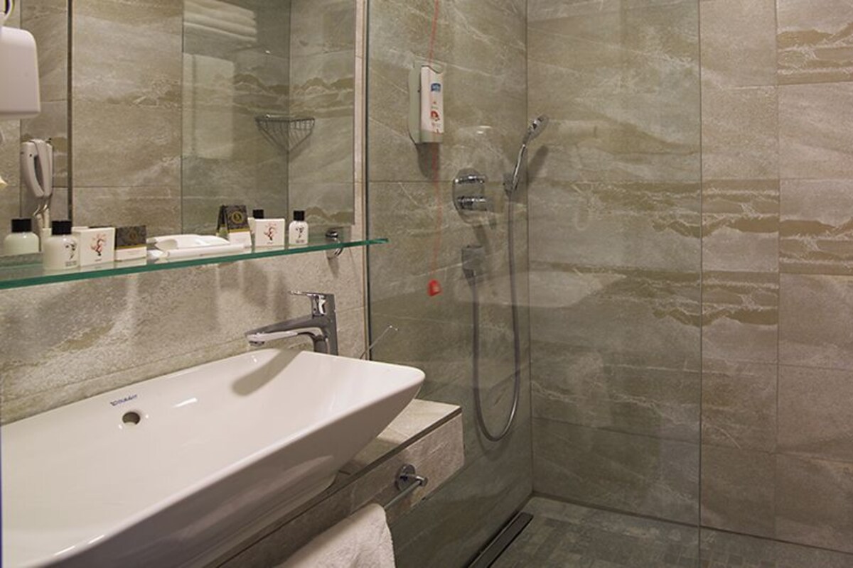 A bathroom with a glass shower enclosure, a sink, and a mirror.