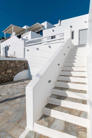 A white staircase leading to a building with stone steps and a stone wall. - Melangel (Mykonos)