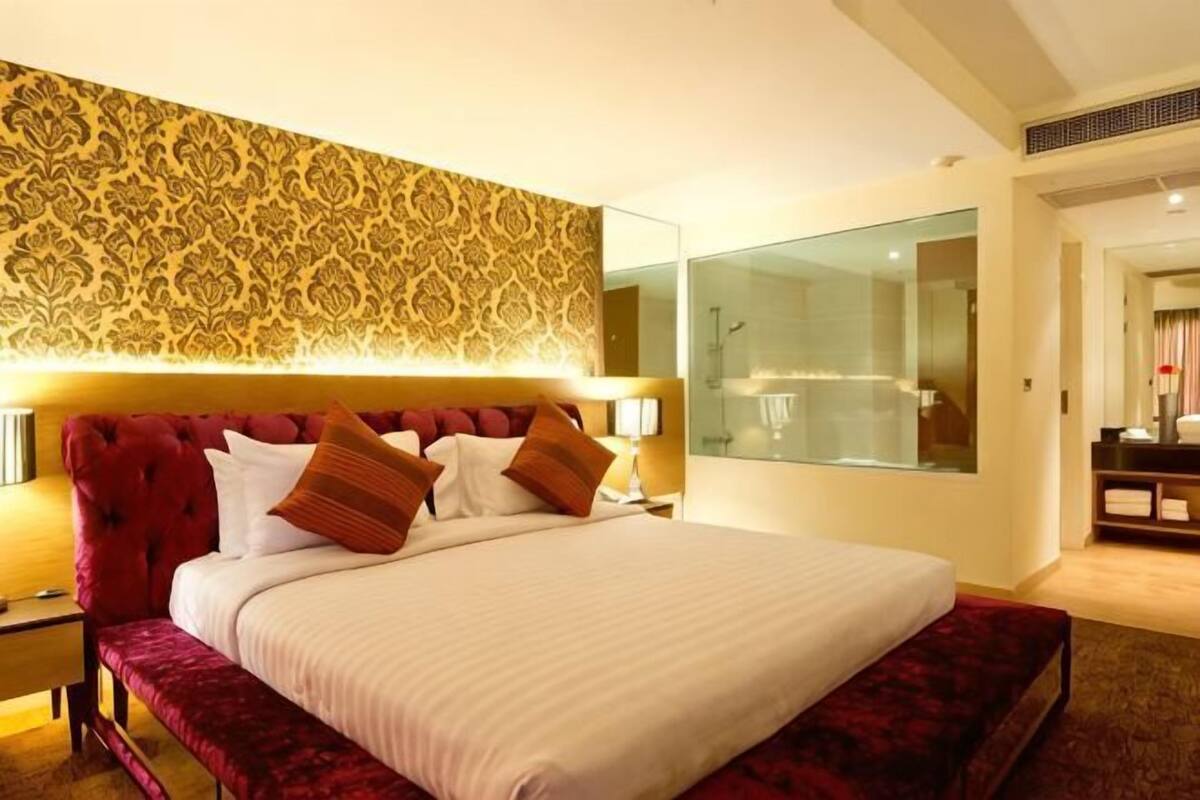 A hotel room with a large bed, a glass shower enclosure, and a patterned wall.