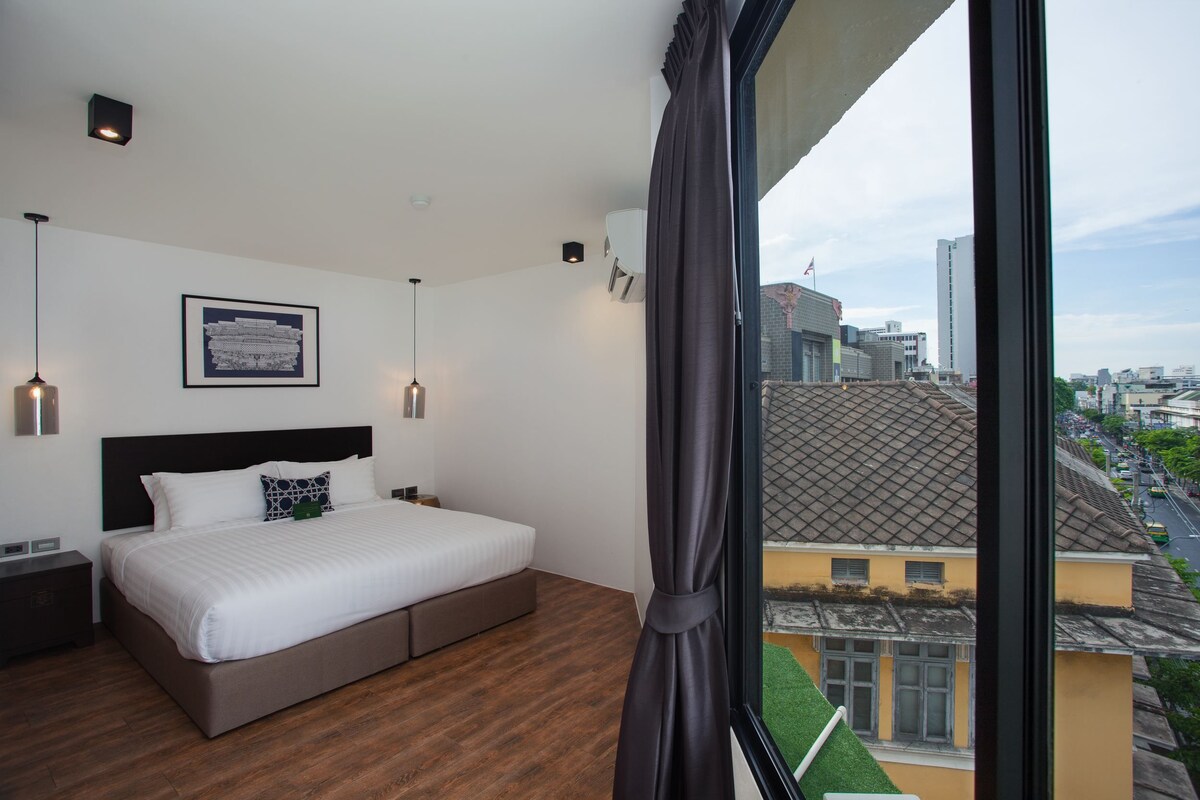 Habitación de hotel moderna con una cama grande, un cuadro en la pared y vistas de la ciudad a través de una ventana.