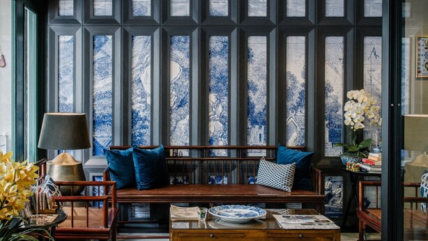 A room with a wooden bench, a table with newspapers, and a vase of flowers. - Oriental Heritage Hotel (Bangkok)