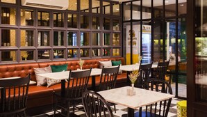 A restaurant interior with a brown leather booth seating area, black chairs, and tables. - Oriental Heritage Hotel (Bangkok)