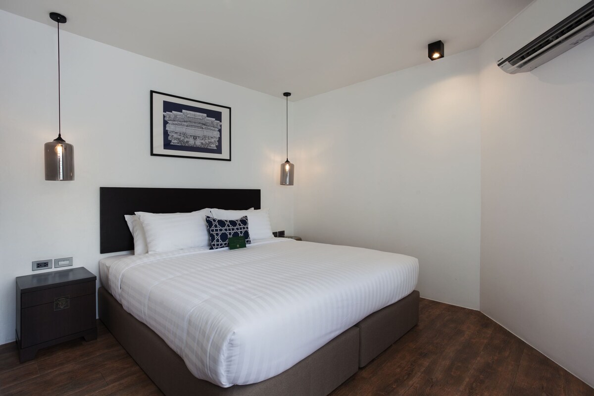 A modern bedroom with a large bed, two bedside tables, a framed picture on the wall, and pendant lights.