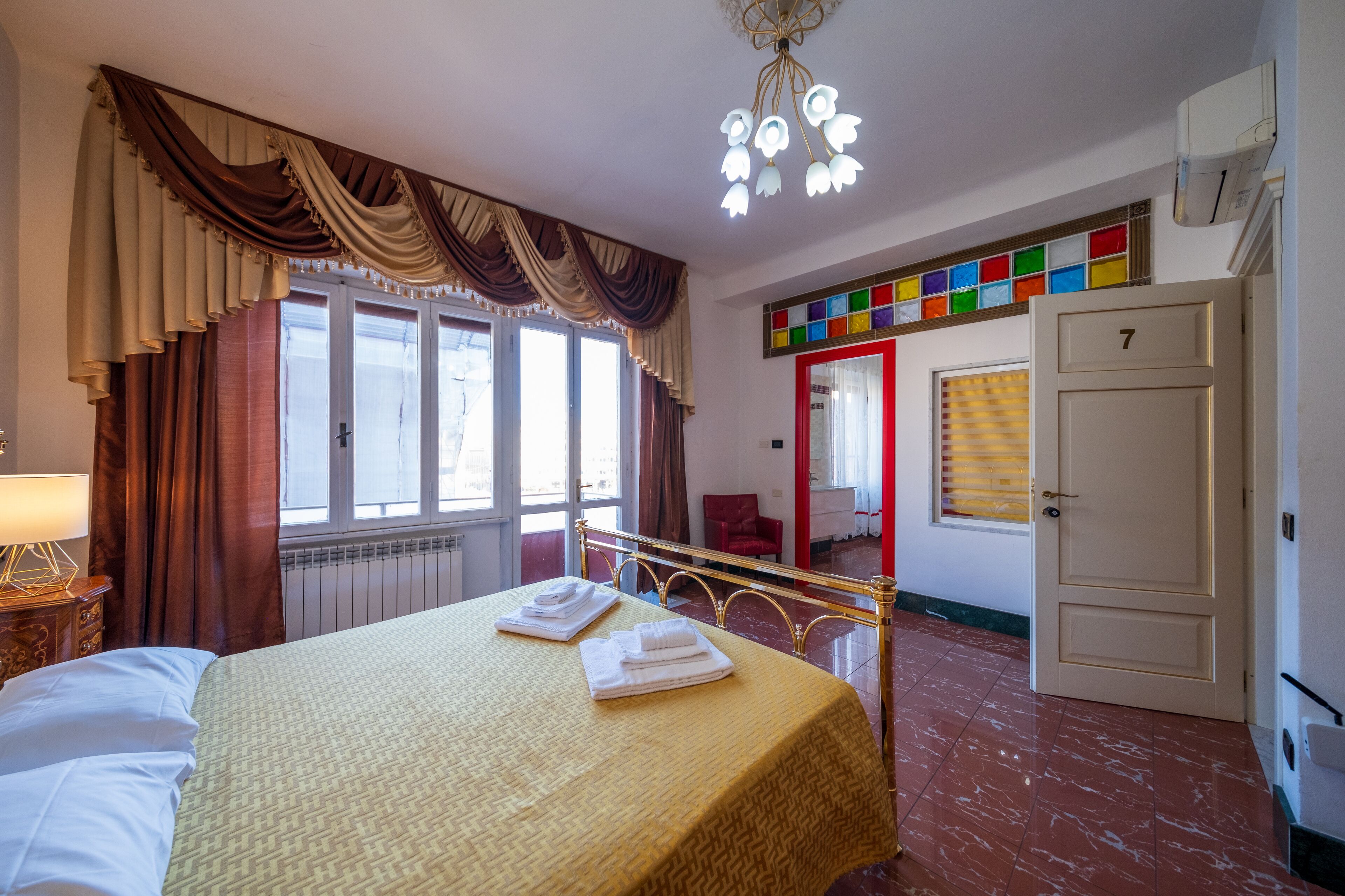A hotel room with a bed, a window with curtains, a mirror, a door, and a radiator.