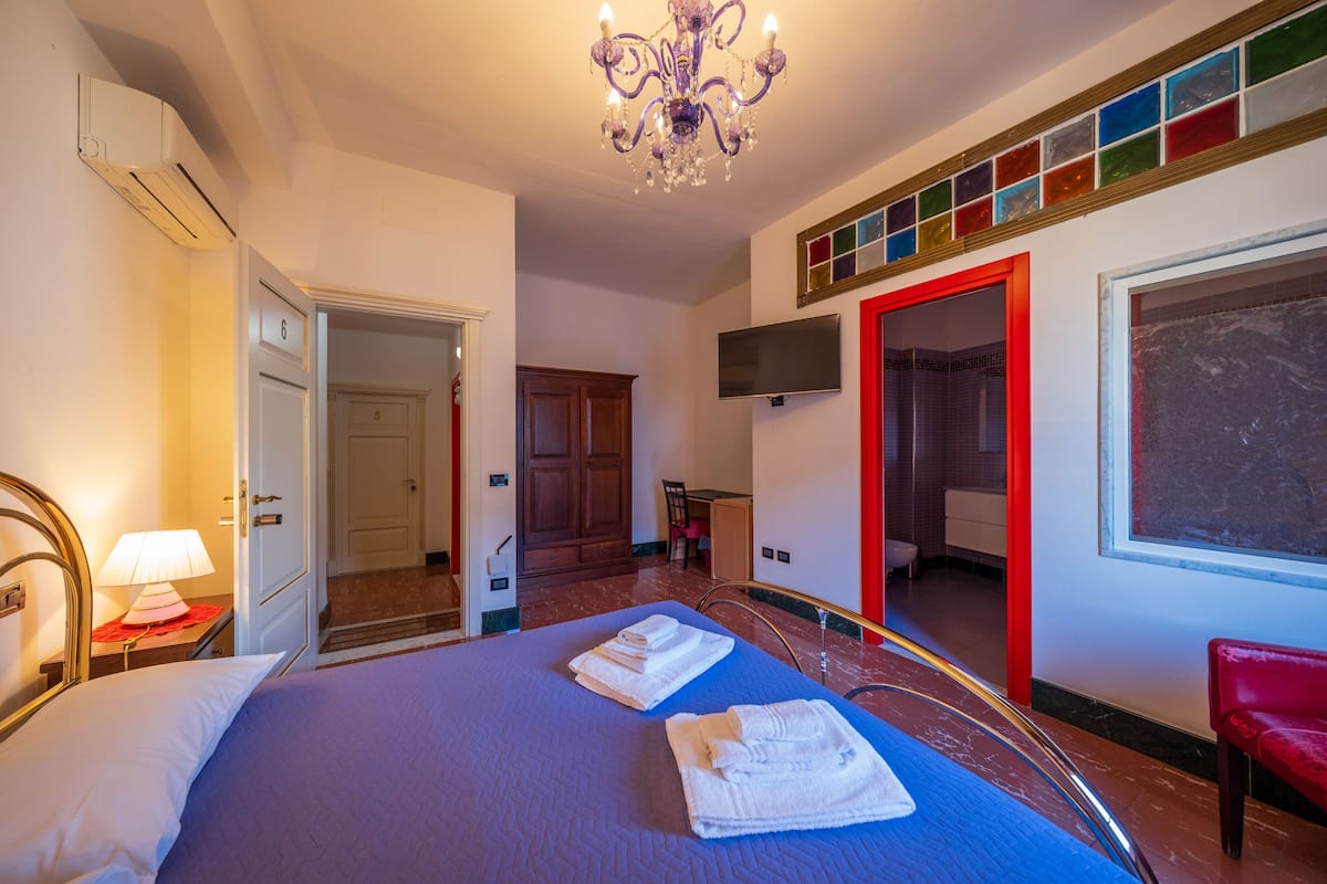 A hotel room with a bed, a desk, a TV, and a red door.