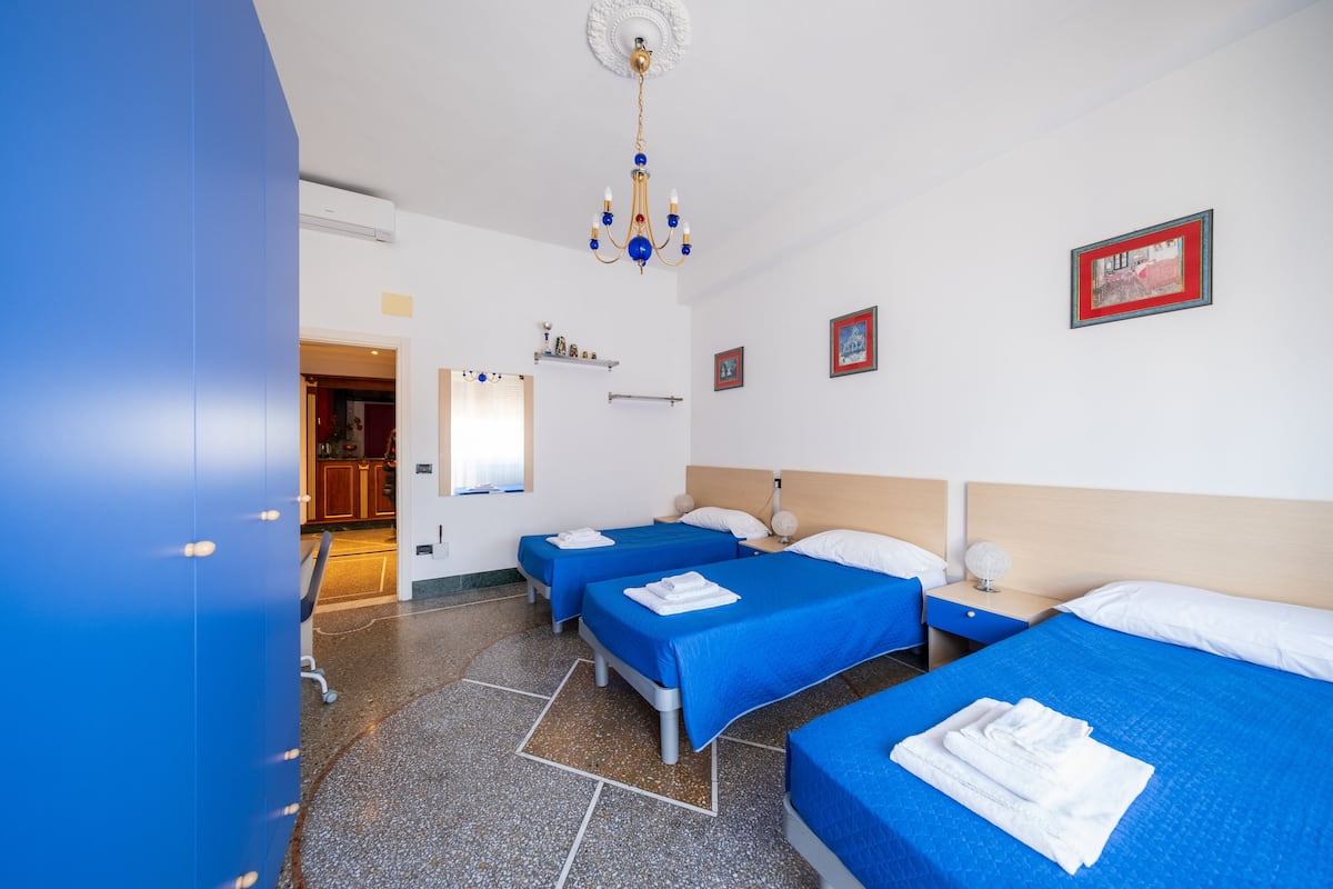 A hotel room with three beds, a chandelier, and a small kitchenette.