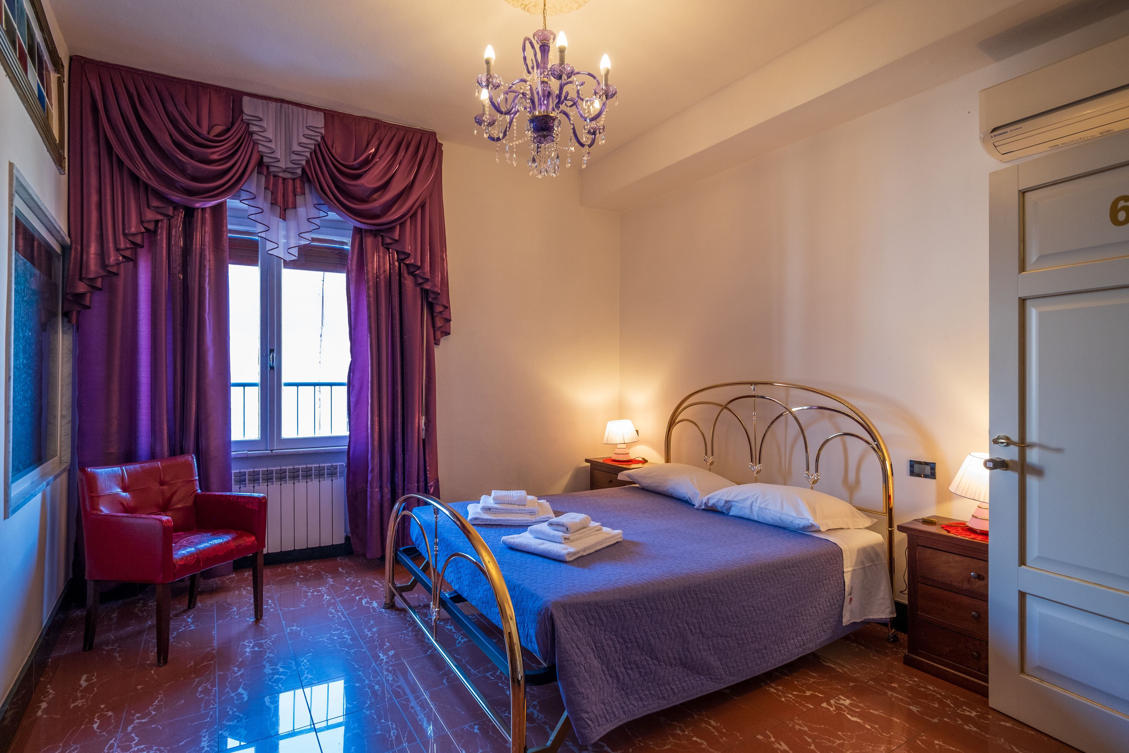Un dormitorio con cama, una silla, un candelabro y un ventanal con cortinas.