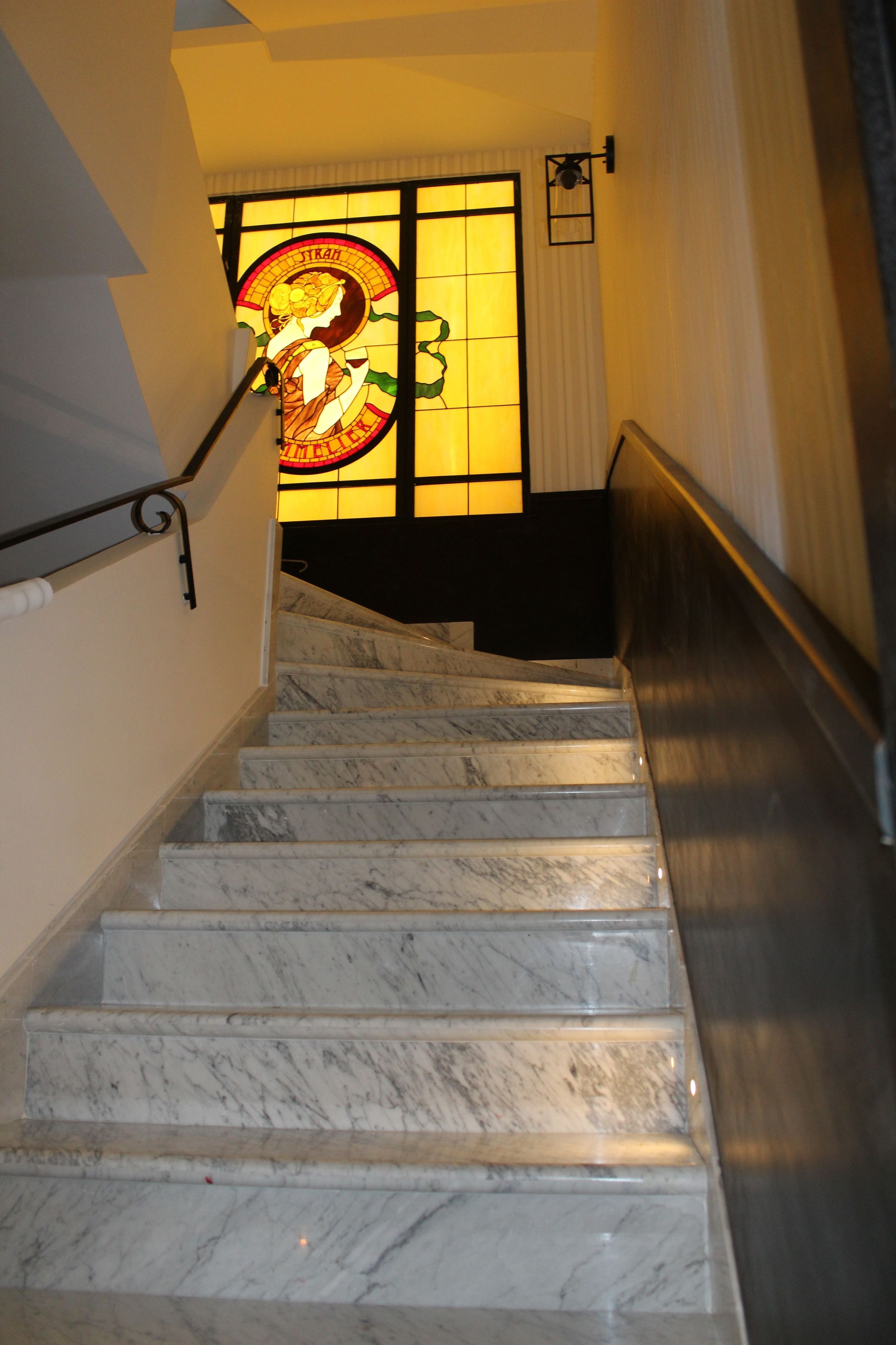 Eine Marmortreppe mit Handlauf, die zu einem Raum mit einem Glasfenster und einer Tür mit Vorhang führt.
