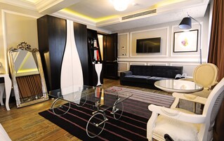 Una sala de estar moderna con una mesa de centro de vidrio, un sofá oscuro, un sillón blanco y un televisor montado en la pared.