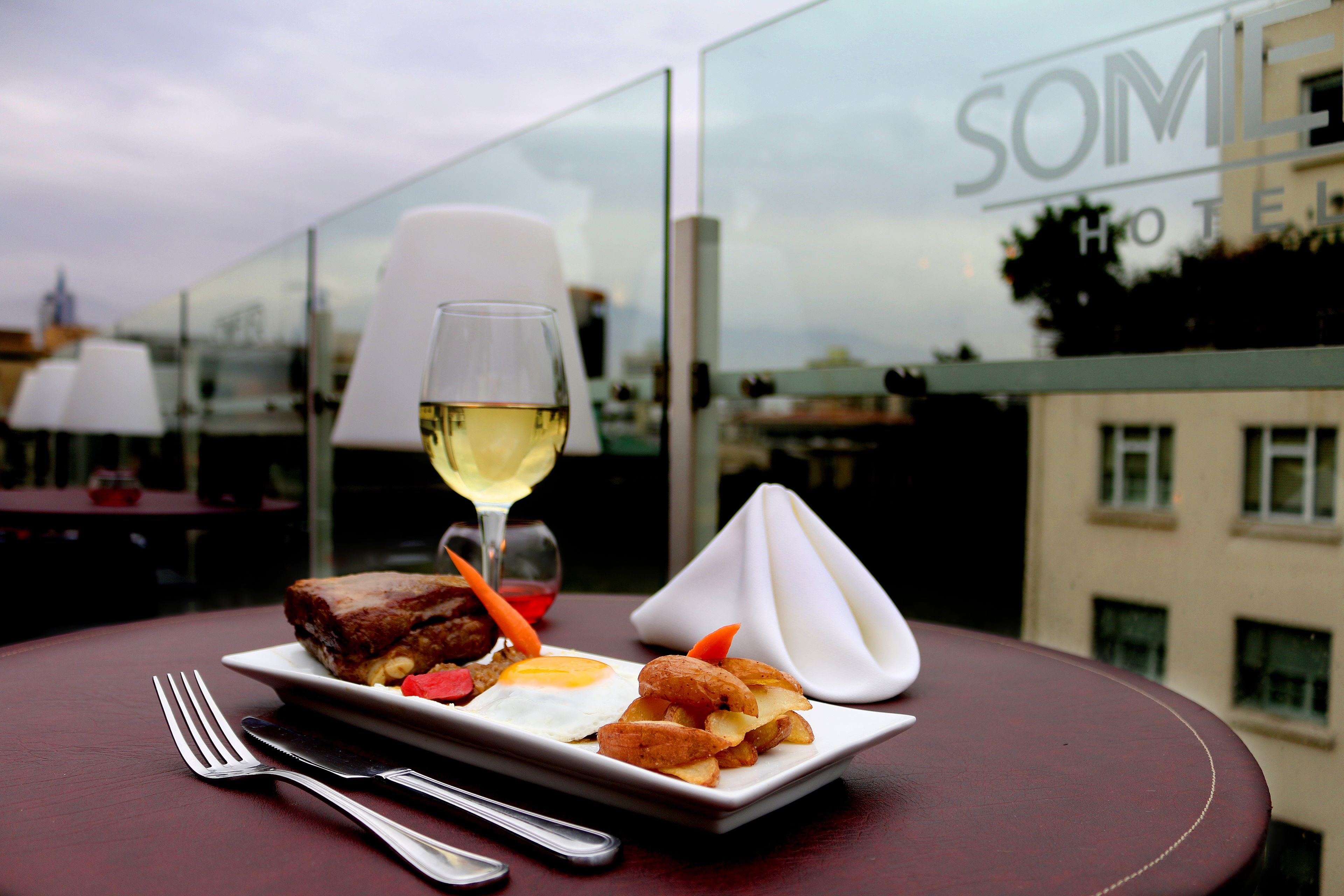 A dining table with a plate of food, a glass of white wine, and a napkin.