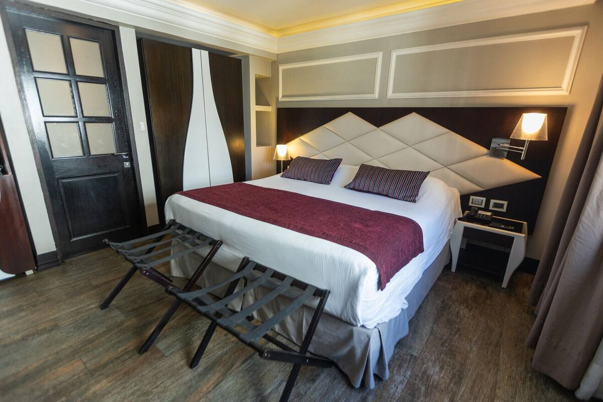 A hotel room with a bed, a desk, a chair, and a door.