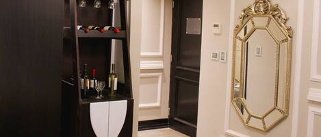 A hotel room with a bed, a wardrobe with bottles and glasses, a door, and a large mirror.