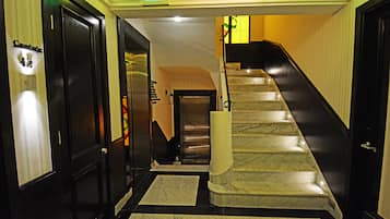 A hotel lobby with a marble staircase, a reception desk, and a sign indicating the exit.