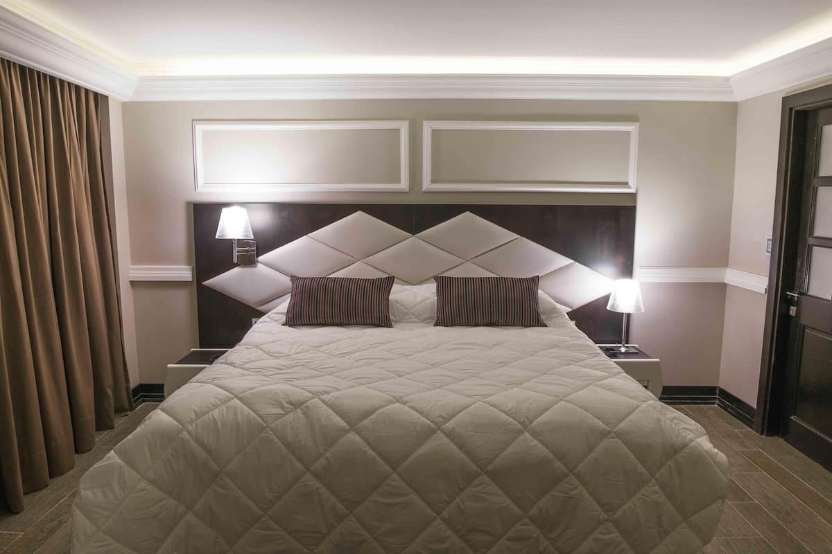 A hotel room with a large bed, two bedside lamps, a headboard with a geometric design, and a door on the right.