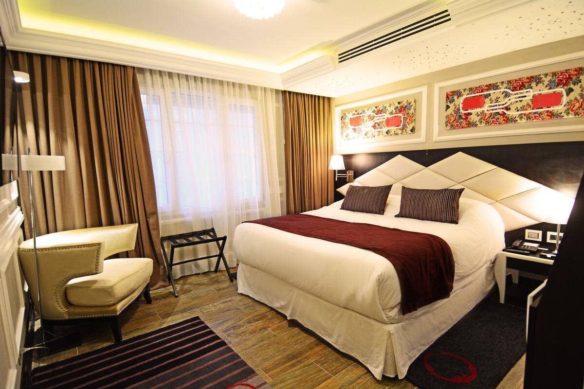 A hotel room with a large bed, a chair, a desk, and a nightstand.