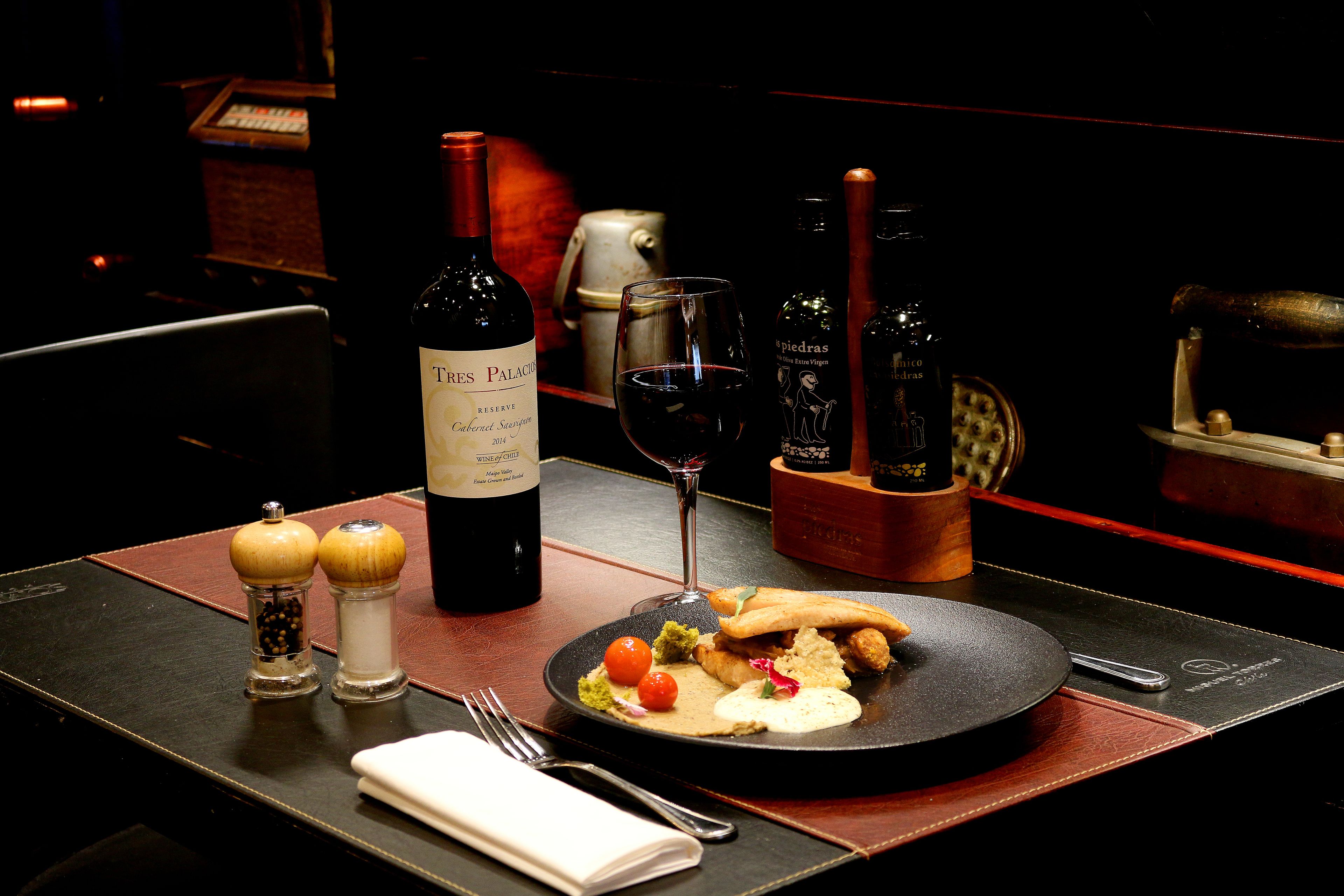 A dining table with a bottle of wine, a glass, and a plate of food.