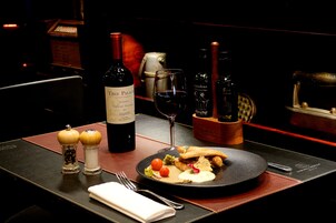 Una mesa de comedor con una botella de vino, una copa y un plato de comida.