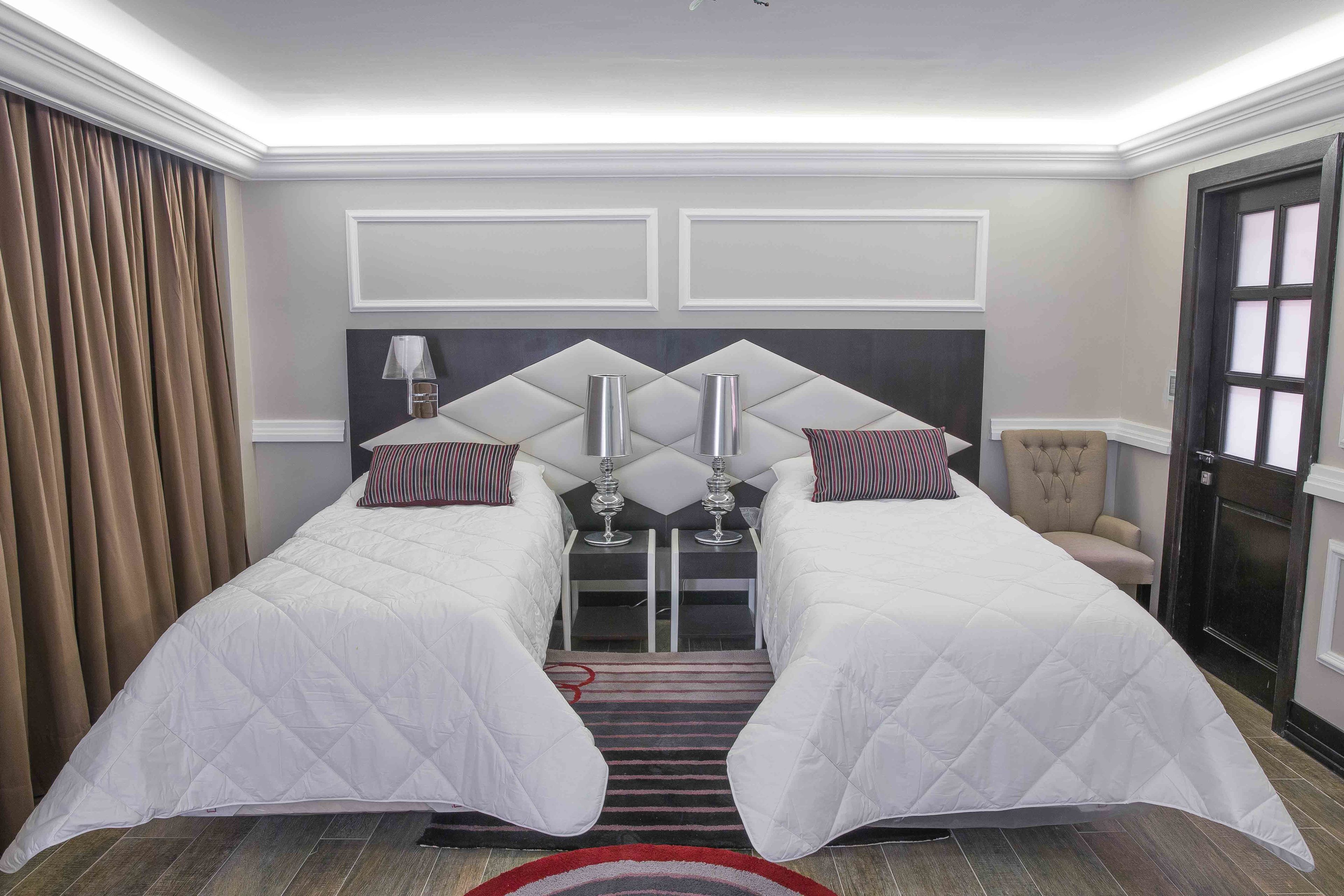 Hotelkamer met twee bedden, een stoel, een klein tafeltje met een lamp en een deur met geëtste glazen panelen.