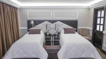 Hotelkamer met twee bedden, een stoel, een klein tafeltje met een lamp en een deur met geëtste glazen panelen.