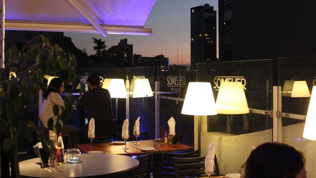 Un bar en la azotea con mesas y sillas, iluminado por lámparas.